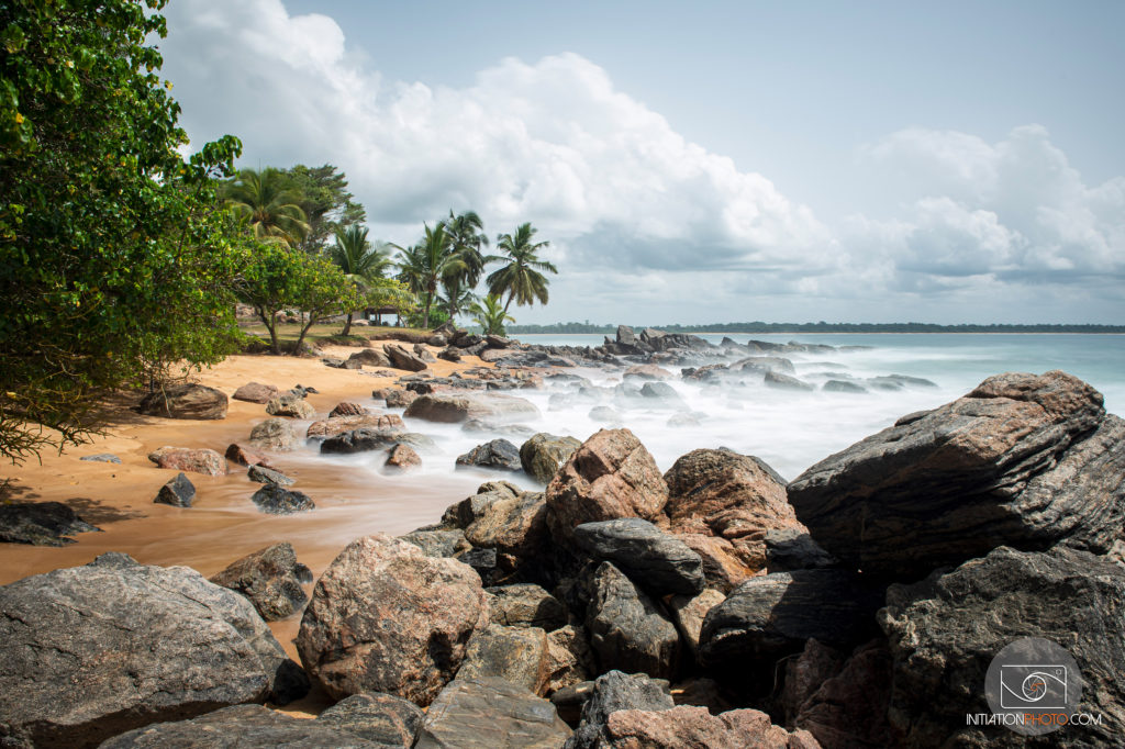 Photo de paysage en couleur représentant une plage de la Baie des Sirènes en Côte d'Ivoire, prise en pose longue la journée (initiationphoto