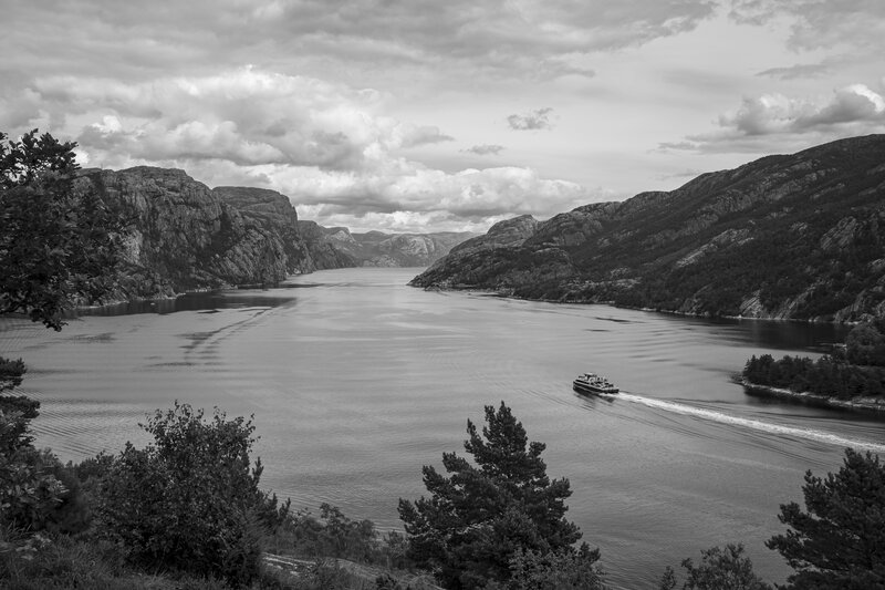 Photo noir et blanc d'un paysage norvégien représentant un fjord entre les montagnes sur lequel circule un bateau