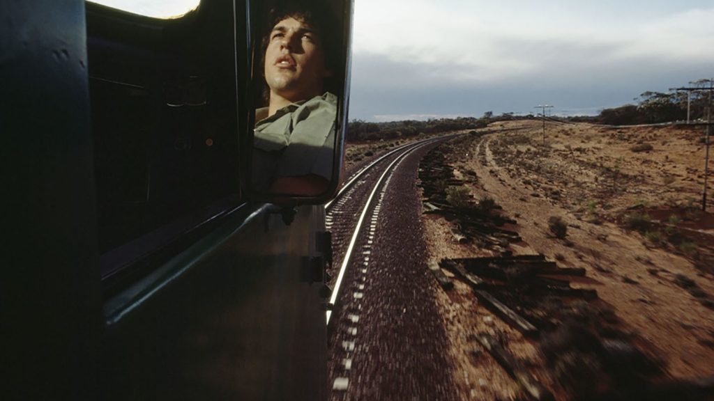 Photo couleur de William Albert Allard représentant le reflet du visage d'un jeune homme dans le rétroviseur d'un train circulant sur des voies dans la campagne (initiationphoto.com)