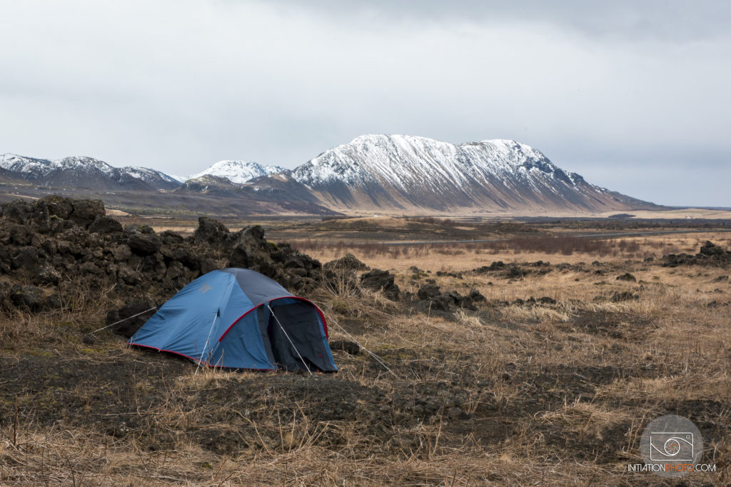 Photo d'un paysage en couleur représentant une tente plantée au milieu de nulle part en Islande avec des montagnes enneigées à l'arrière-plan (initiationphoto)
