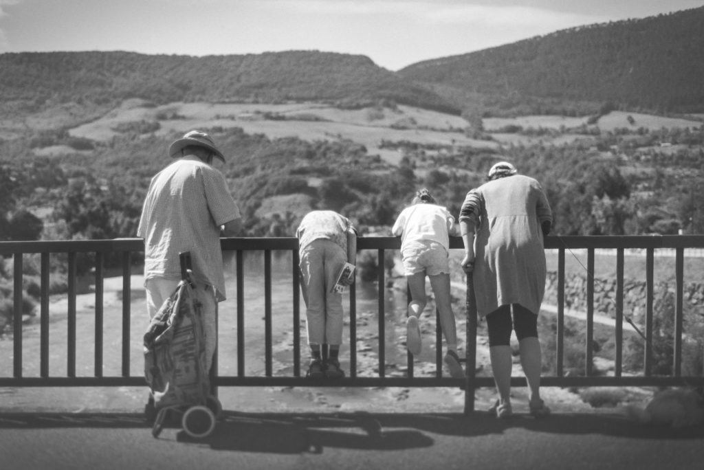 Photo argentique en Noir & Blanc, d'une famille de 4 personnes de dos sur un pont regardant vers la rivière