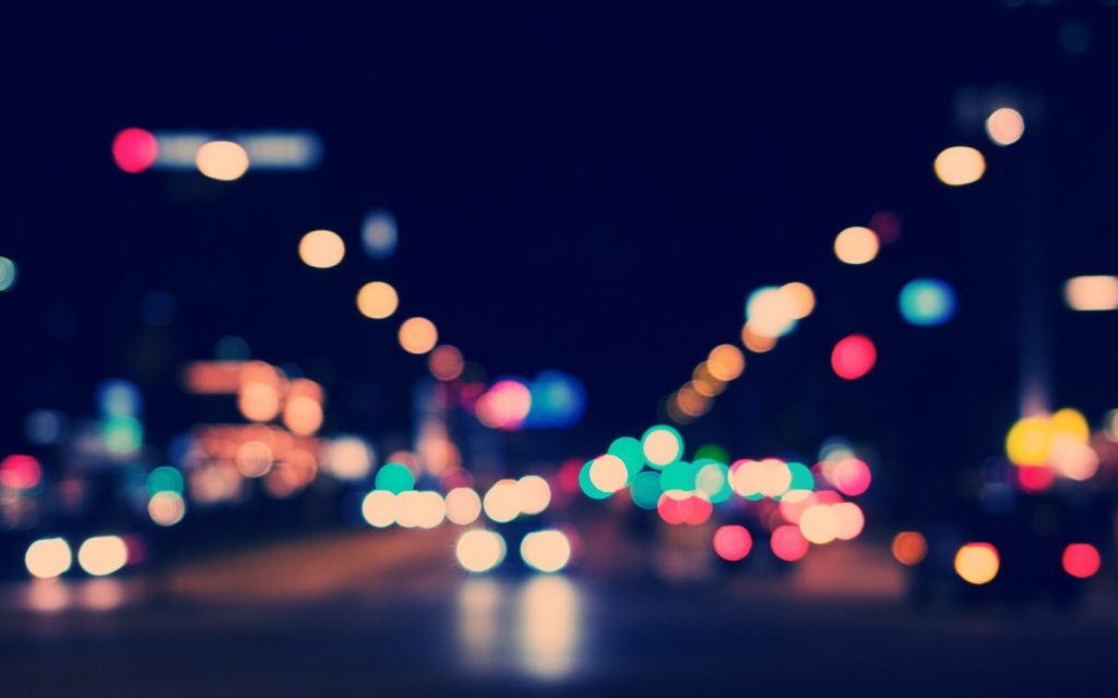 Photo floue en couleur d'une rue avec des voitures et des éclairages publiques, créant des ronds lumineux
