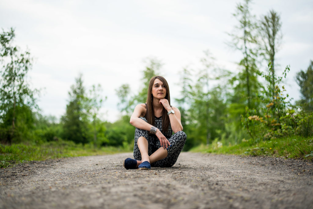 Photo de portrait en couleur représentant une jeune femme assise sur un chemin dans la nature