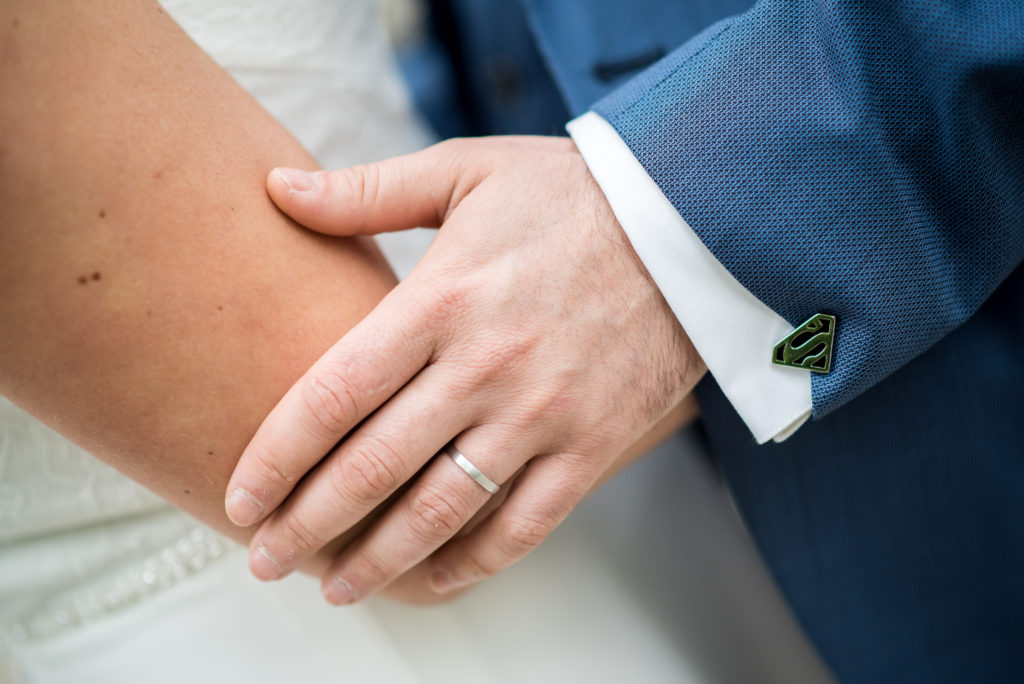 Photo en couleur de la main d'un marié et de son bouton de manchette superman